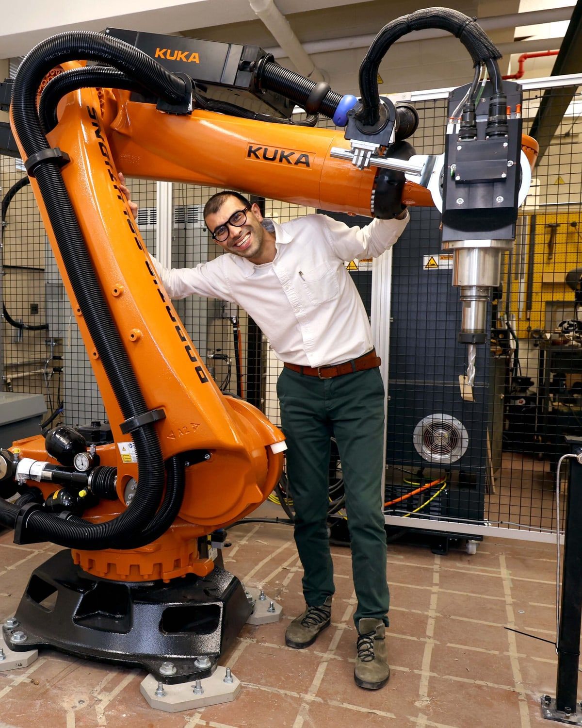 A smiling engineer leans against a large orange industrial robot arm