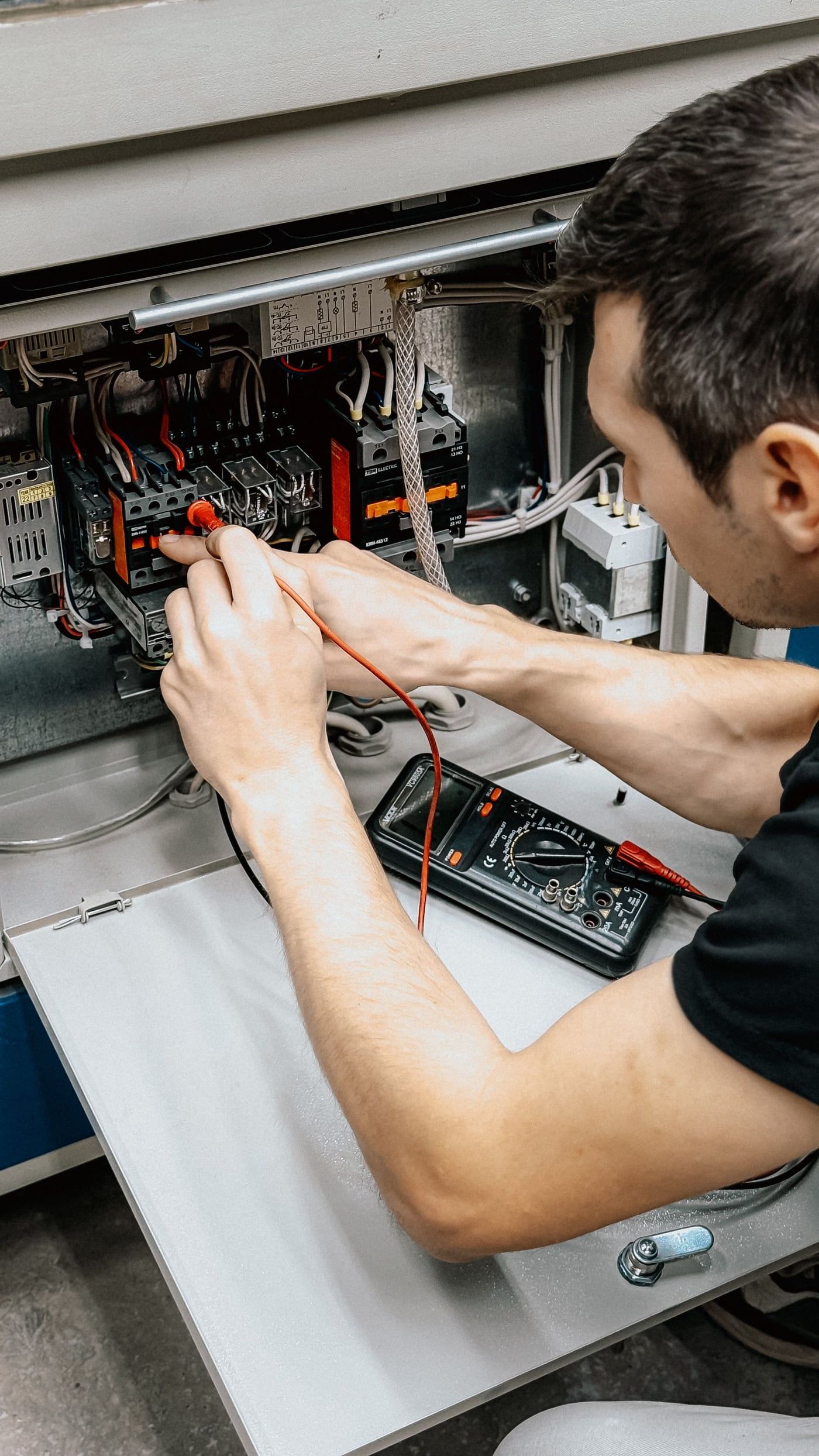 A technician tests the wiring inside an open machine control cabinet with a multimeter